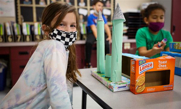 Student holds up a castle made out of recycled materials